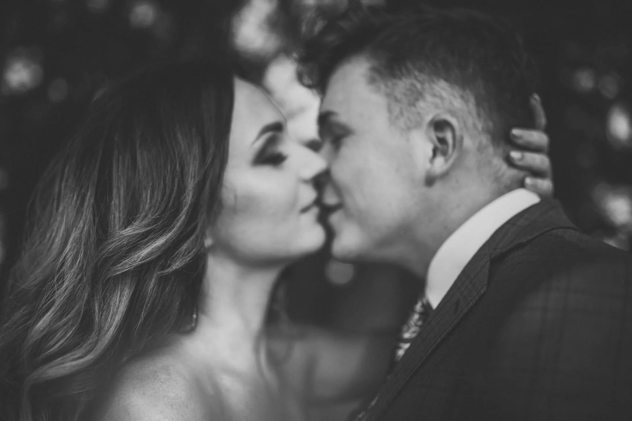 Rozmyte światła w tle podkreślają bliski pocałunek pary trzymającej się za dłonie